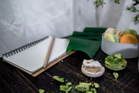 Crushed pastel, orange and green macaroons on a wood background with whole one in white plate with jug with flowers on the backの写真素材