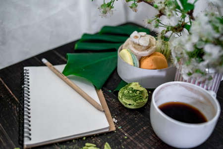 Crushed pastel, orange and green macaroons on a wood background with whole one in white plate with jug with flowers on the backの写真素材