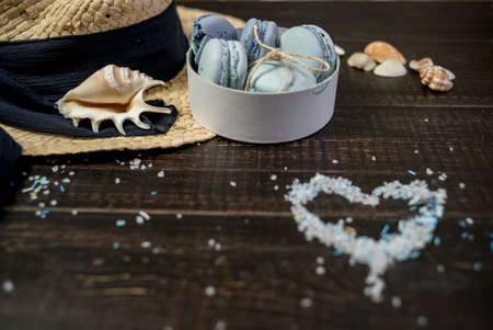 Straw hat with blue macaroons and sea salt with shells on the wood backgroundの写真素材