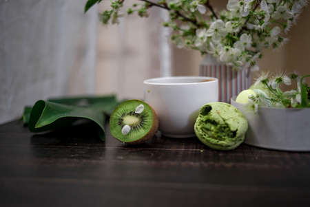 Green and beige macaroons tied with a tourniquet against the background of cherry blossom branches on a wooden tableの写真素材