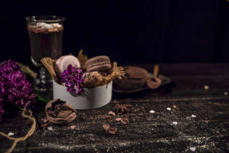 Hot chocolate (cocoa) in a glass mug with two tubes for drinking.There are some macarons on a linen napkin on the wood table with some lilacの写真素材