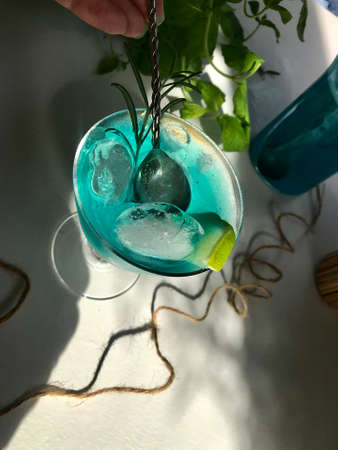 Blue cold drink in a glass with ice cubes on white desk with blue background. Also used mint leaves and rosemary, rope, spoon  with natual sunlight from the open windowの写真素材