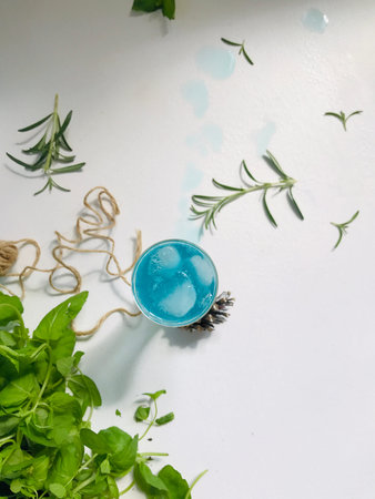 Blue cold drink in a glass with ice cubes on white desk with blue background. Also used mint leaves and rosemary, rope, spoon  with natual sunlight from the open windowの写真素材
