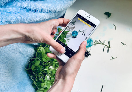 Person taking picture of blue colored drink on smartphone/ Drink is on white background surrounded...