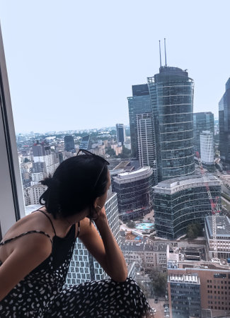 Young beautiful woman sitting on the roof of a skyscraper and looking out the windowの写真素材