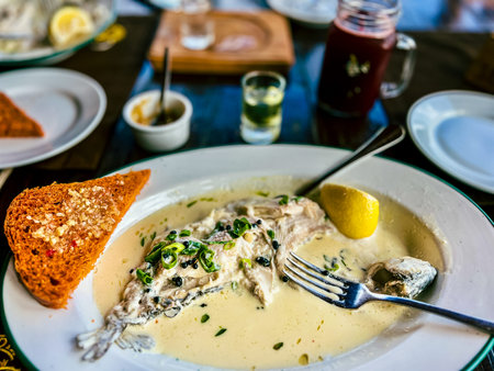 Fried Golden trout fish with lemon and herbs in a white plate on a wooden table at the restaurant in...
