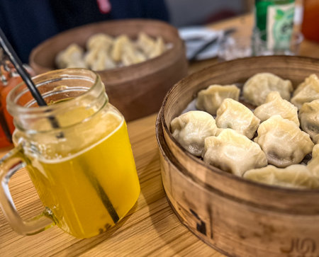 Steamed dumplings in wooden bamboo steamer like a plate with a glass of juiceの写真素材
