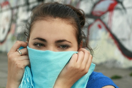 Young beautiful brunette hiding behind a blue scarfの写真素材
