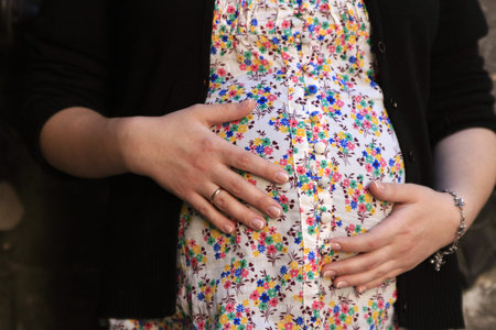 Pregnant woman in colored blouse hugging arms stomach
