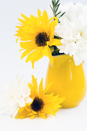 Yellow jug with yellow and white flowers on a light backgroundの写真素材