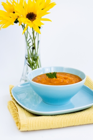 	Pumpkin soup in a blue plate and a bouquet of yellow flowersの写真素材
