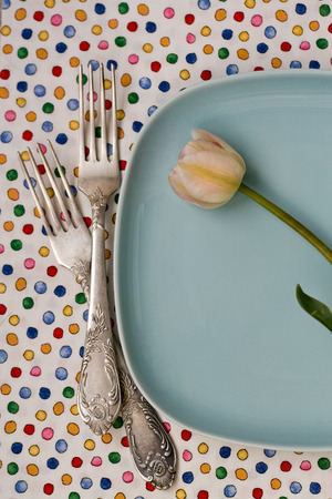 The two dessert forks lying next to a plate of tulips on a colorful tableclothの写真素材