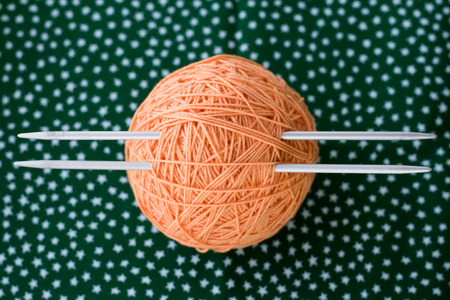 A bright orange ball of yarn and needles for knitting lying on a green backgroundの写真素材