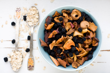 Blue plate with dried apples and berries and a spoon of oatmeal on a white wooden background. Healthy food.の写真素材