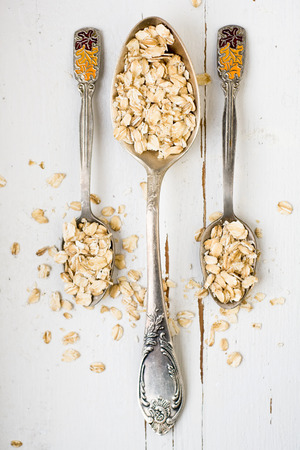 Three tablespoons of oatmeal lying on a white wooden background. Healthy food.の写真素材