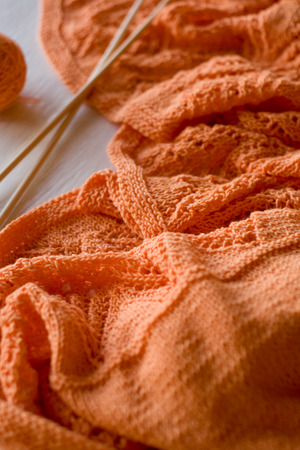 Bright orange plaid knitted, knitting needles and yarn balls on a white wooden backgroundの写真素材