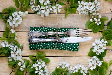 Fork and knife lying on a wooden background among the branches of a flowering tree