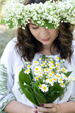 Portrait of a young beautiful in traditional Ukrainian embroidered shirt and a wreath of lilies of the valley on the headの写真素材