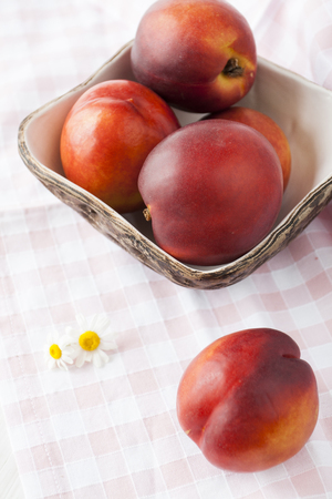 Juicy ripe nectarines lie in a hand-made plate on a tablecloth in a cellの写真素材