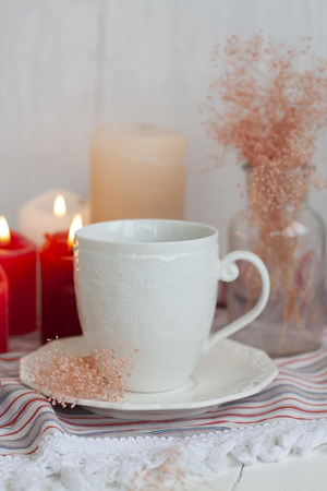 A hot cup of black tea on a striped tablecloth, wax candles, a glass vase with decorative herbs on a white background.の写真素材