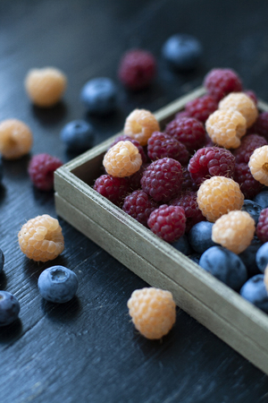 A tasty and healthy snack: a box of raspberries and blueberries on the black background.の写真素材