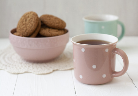 A tasty snack: two cups of black tea and a bowl of oatmeal cookies on the white background.の写真素材