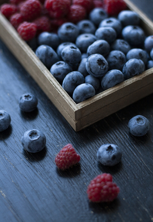 A tasty and healthy snack: a box of raspberries and blueberries on the black background.の写真素材