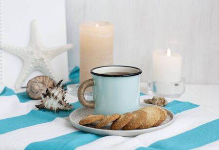 A study break: a hot mug of black tea with homemade cookies on a striped tablecloth; wax candles, decorative starfish, seashell, pile of notebooks on a white background.の写真素材