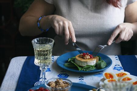 A gourmet dinner: a plate of grilled camembert with spinach, walnuts and smoky tomatoes, various appetizers and a glass of wine on a decorative tablecloth.の写真素材