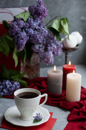 Atmospheric photo: black coffee and a white cup, a bouquet of lilacs, a few large candles, marshmallows on a gray backgroundの写真素材