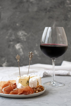 Crystal glass with red wine, in the foreground a plate with ham, nuts, crackers and Camembert...