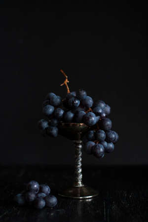 A bunch of dark blue grapes lies in a silver bowl. Composition on a black backgroundの写真素材