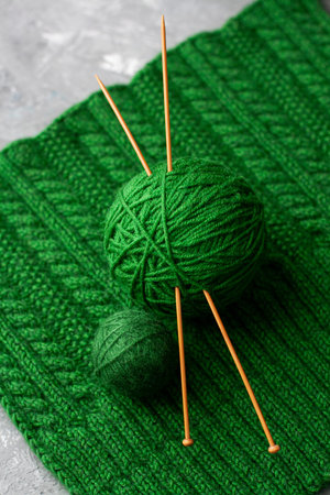 Two green balls of yarn with two knitting needles on green knitted texture backgroundの写真素材