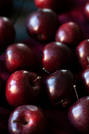 Closeup many dark red apples on black wood and dark red fabric