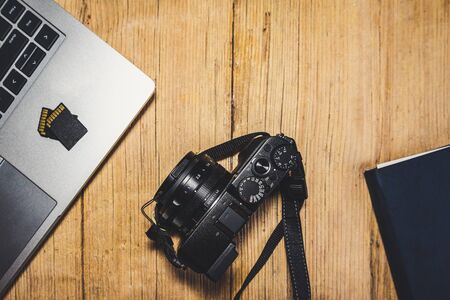 Wooden desk table with camera, laptop, memory cards and clipboard. View from top.の写真素材