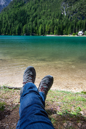 Trekking legs of a man lying on the shore of a lake enjoying the mountain landscapeの写真素材