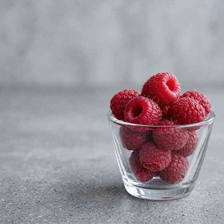 Ripe raspberries in a glass bowl on a gray background