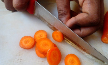Female cook cutting fresh carrot vegetables for cooking at kitchen home