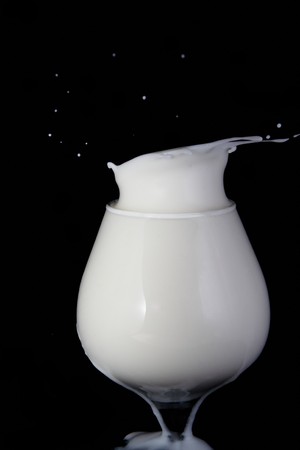 Splash milk in the glass on the black backgroundの写真素材