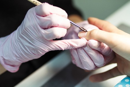 The master paints a varnish with the help of a brush on the nails of a personの写真素材