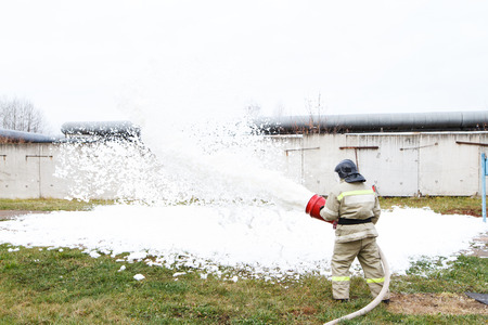 Firefighters extinguish the fire with a chemical foam coming from the fire engine through a long hoseの写真素材