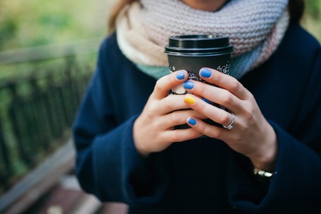 Girl in autumn coat holding a glass of coffee in the streetの写真素材