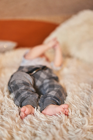 Baby legs in blue pants lying on a bed with a napの写真素材