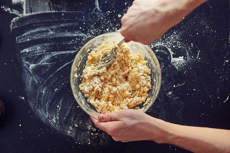 Unrecognizable male cook stirs the filling for the cake on a dark table, close-up. Top view. Top view. A hand holding a pan of food. High quality photo.の写真素材