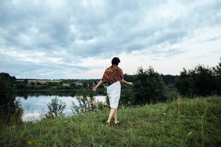 A girl runs along a lush green field to a pond. High quality photoの写真素材