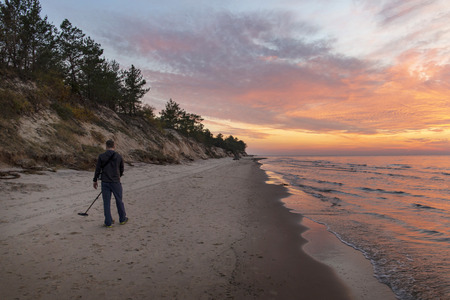 Treasure hunter with metal detector on sunset beachの写真素材