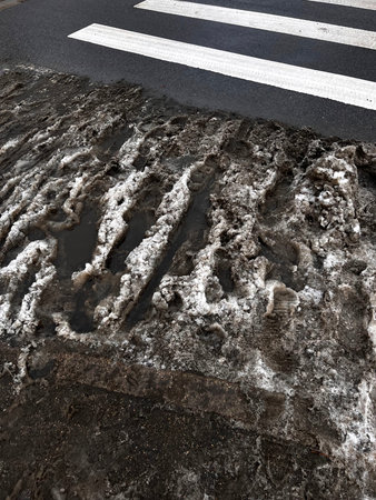 Dirty melting snow and slush on a city street near a pedestrian crossing. Close-up of muddy winter...