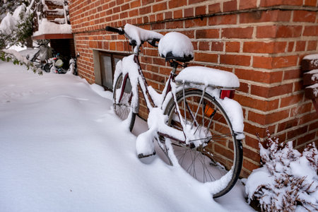 A snow covered bicycle against the backdrop of a red brick houseの写真素材