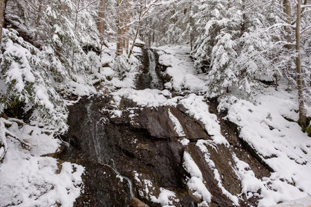 Snow covered river and waterfall with mountains in winterの写真素材