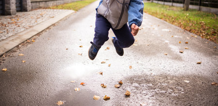 A child jumps over a puddle of water and leaves - the road in the backgroundの写真素材